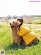 A woman in a yellow jacket sitting next to a dog in a field.