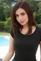 A woman in a black shirt and jeans posing by a pool.