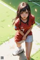 A girl in a red shirt and white shorts standing on a soccer field.