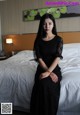 A woman in a black dress sitting on a bed.