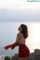 A woman in a red dress standing on a balcony overlooking the ocean.