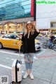 A woman standing on the sidewalk with a suitcase.