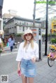 A woman in a white shirt and a denim skirt is walking down the street.
