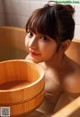 A woman sitting in a bathtub with a wooden bowl of water.