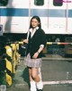 A woman in a school uniform standing in front of a train.