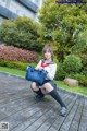 A woman in a school uniform sitting on a wooden bench.