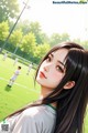 A girl with long black hair standing in front of a soccer field.