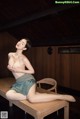 A naked woman sitting on a wooden bench in a room.