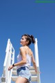 A woman in a white tank top and denim shorts standing on a ladder.