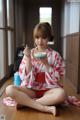 A woman in a red and white kimono sitting on the floor eating a bowl of food.