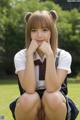 A young woman in a school uniform sitting on the grass.