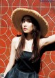 A woman wearing a straw hat leaning against a wall.