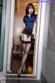 A woman in a blue shirt and black stockings posing in a doorway.